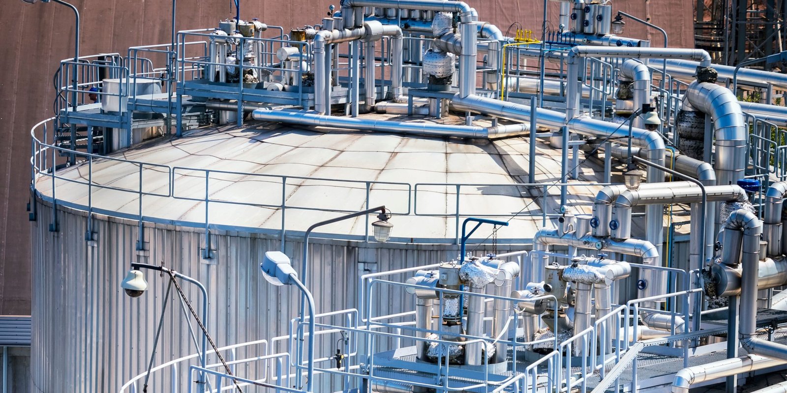Insulated piping and access platforms surrounding a large industrial storage tank.