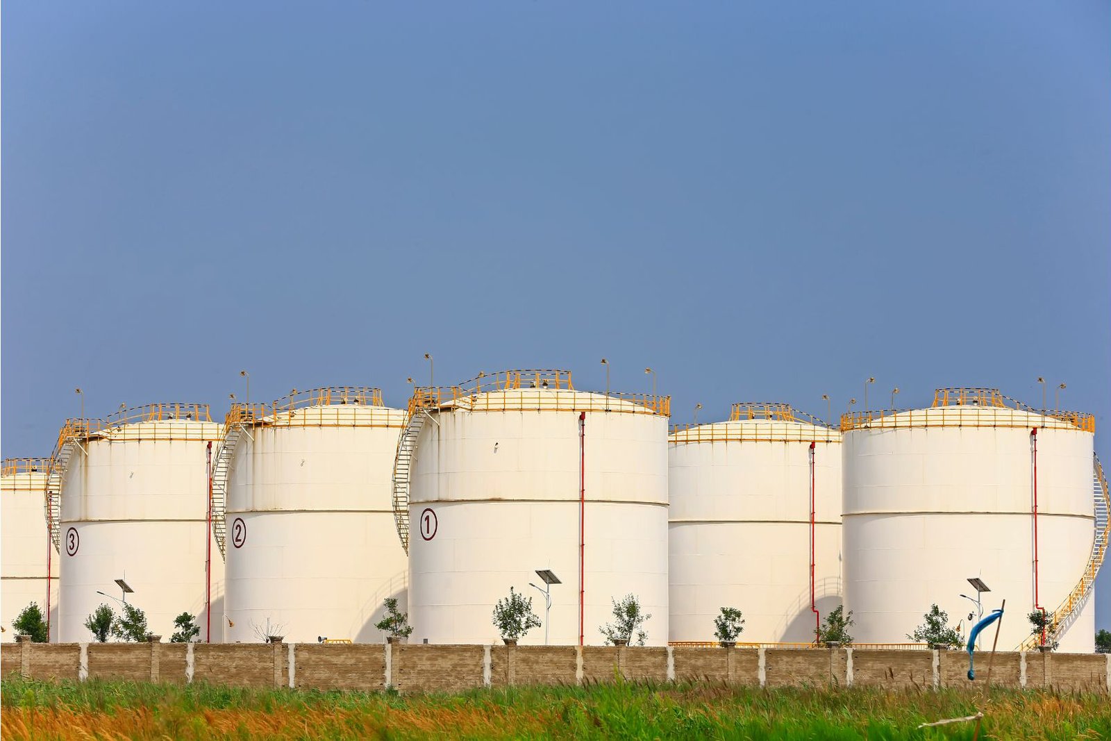 Row of white cylindrical storage tanks with external stairways at an industrial site.