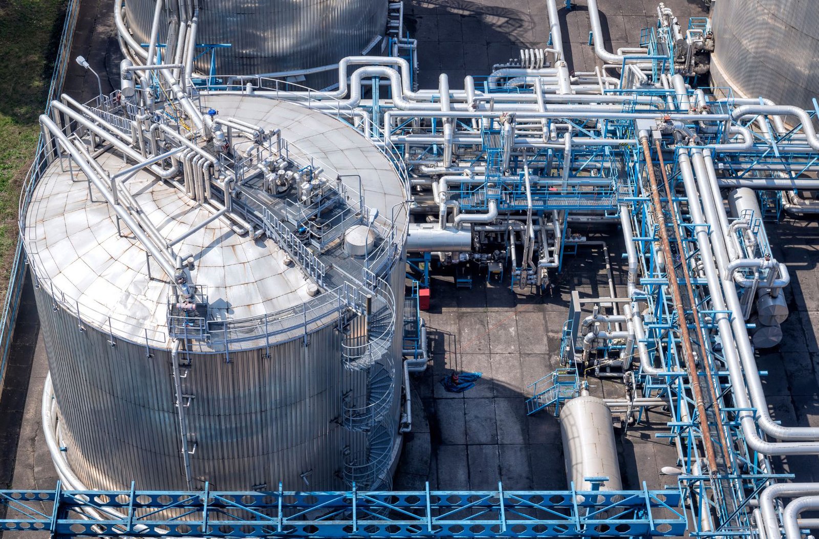 Overhead view of a storage tank surrounded by dense process piping and access platforms.